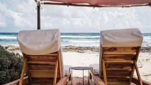 Two wooden lounge chairs with cushions facing a beach. - VILLAS MIA FRONT BEACH  (Xpu-Ha)