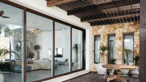 A modern patio with a stone wall, large sliding glass doors leading to a living area, and a wooden table. - VILLAS MIA FRONT BEACH  (Xpu-Ha)