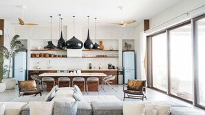 A modern kitchen with a central island, bar stools, pendant lighting, and a large window providing natural light. - VILLAS MIA FRONT BEACH  (Xpu-Ha)