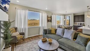 A living room with a sofa, a coffee table, and a view of a mountainous landscape through large windows. - Family Friendly 5BR Mountain Views & Game Room with AC (Superior)