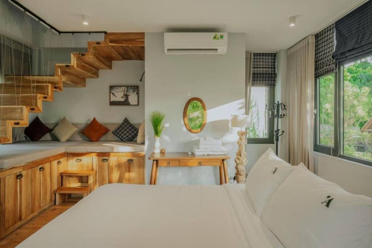 Ein modernes Schlafzimmer mit einer Holztreppe, einem Bett mit weißer Bettwäsche, einem kleinen Tisch mit Pflanze und einer Wand-Klimaanlage.