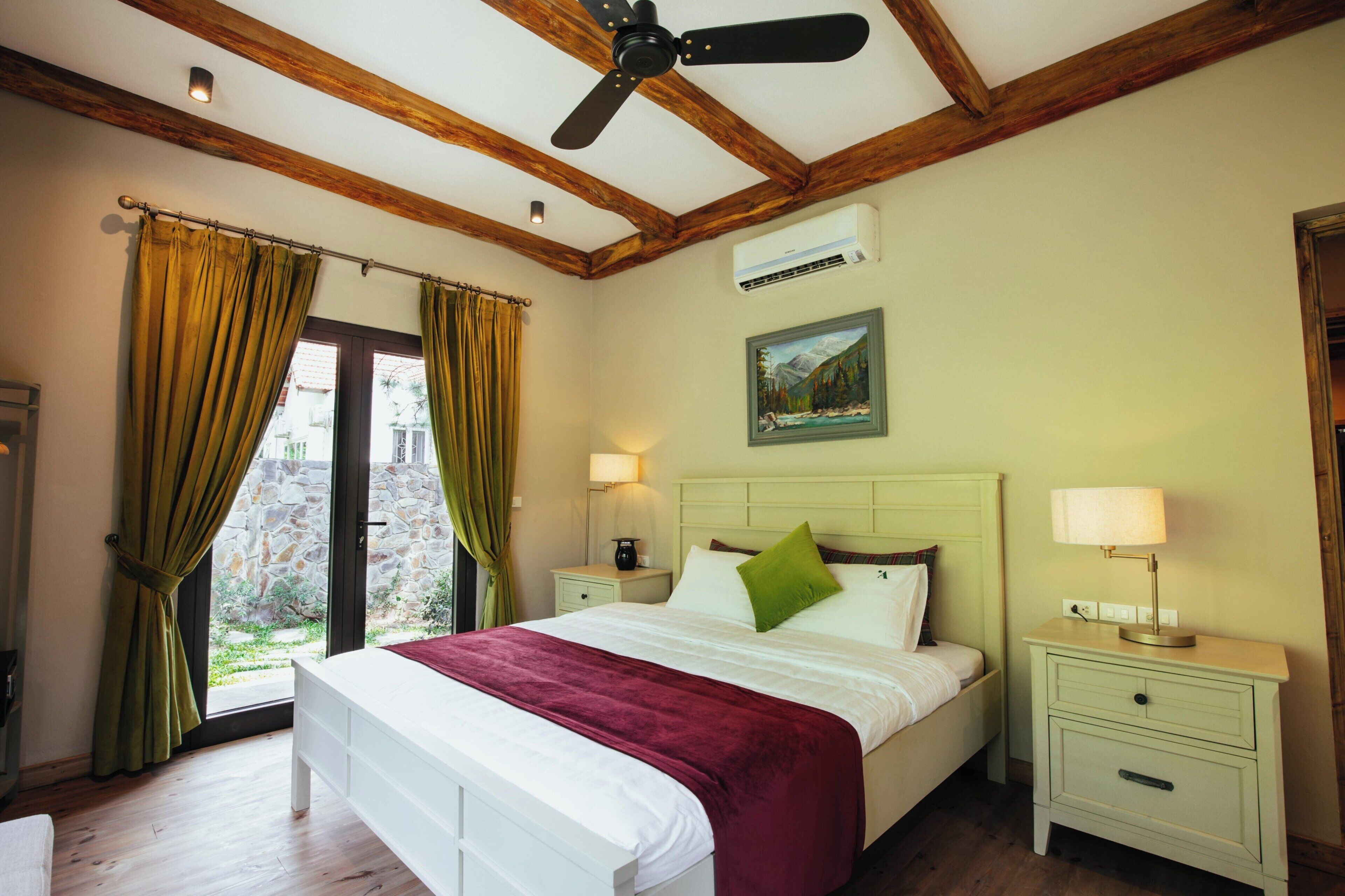 A bedroom with a bed, nightstands, a ceiling fan, a painting, and a window with curtains.