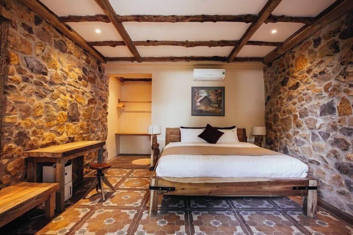 Ein Schlafzimmer mit Stehwänden, Holzbalken, einem Bett, einem Schreibtisch und einem Stuhl.