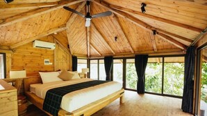 A wooden cabin bedroom with a bed, ceiling fan, and large windows. - Amaya Home Lodge, SPA & Restaurant (Hanoi)