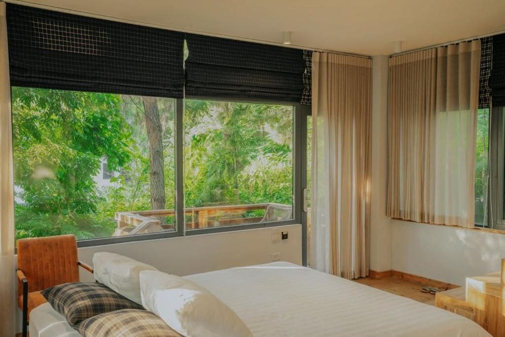 A bedroom with a large window, a bed, a chair, and a wooden desk.