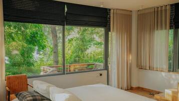A bedroom with a large window, a bed, a chair, and a wooden desk.