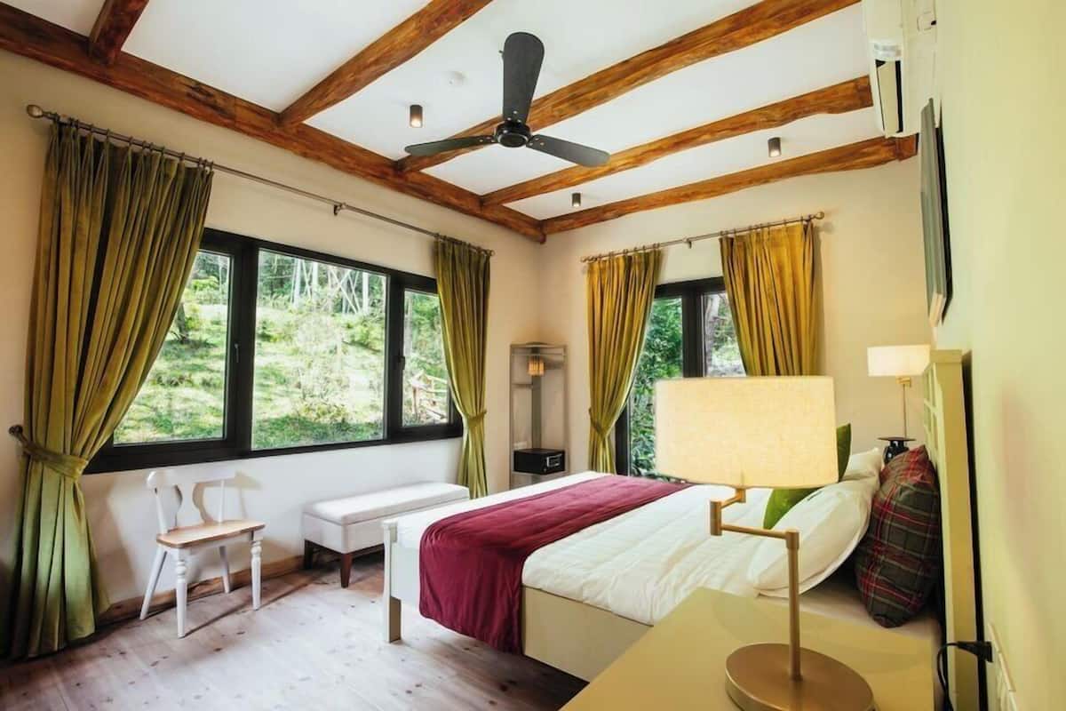 Ein Schlafzimmer mit einem Bett, einem Schreibtisch, einem Sessel, einem Deckenventilator und großen Fenstern mit Vorhängen.