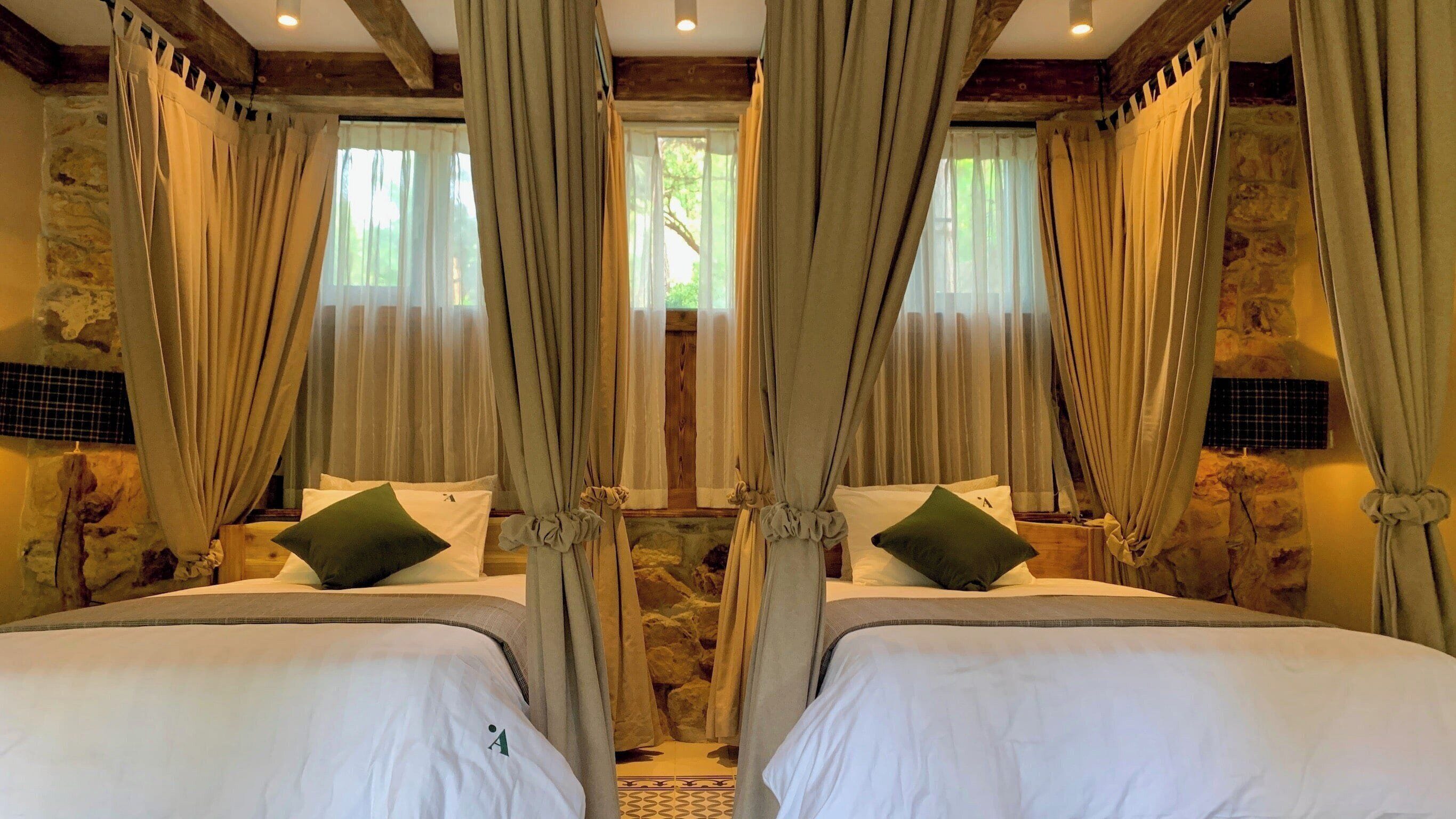A room with two beds, stone walls, and curtains.
