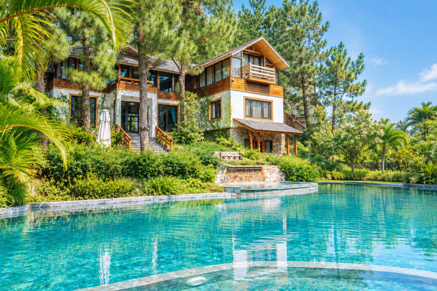 Une maison à deux étages avec une piscine, entourée d’une végétation luxuriante et de pins.