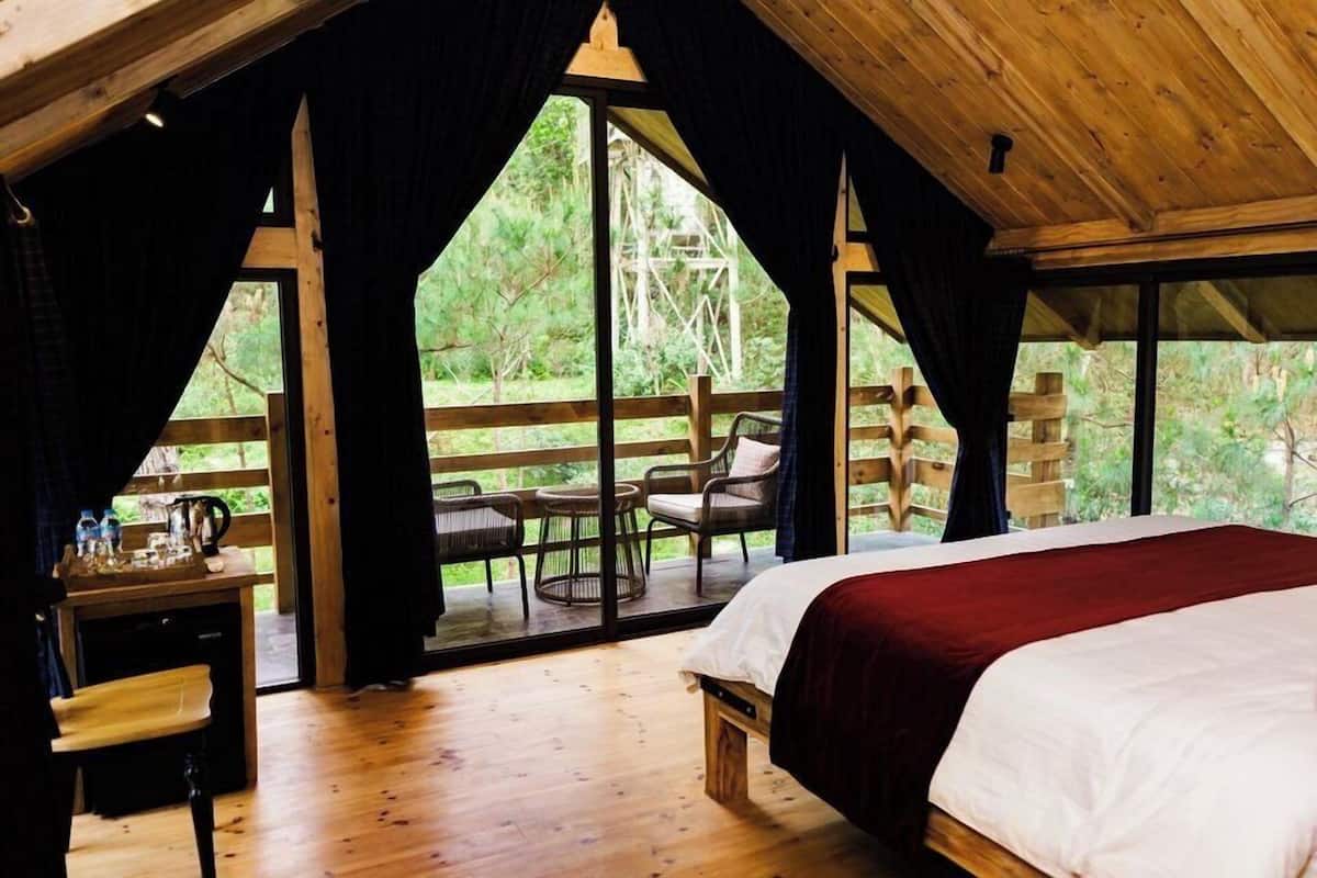 Ein Zimmer mit Holzboden, einem Bett, einem Tisch und Stühlen neben einem großen Fenster.
