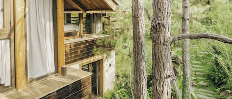 A wooden cabin with a balcony overlooking a garden and forest.