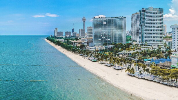 A coastal cityscape with high-rise buildings, a beach, and a prominent tower. - Avatara Beachfront - Best Rooftop Pool & Ocean Views (Pattaya)