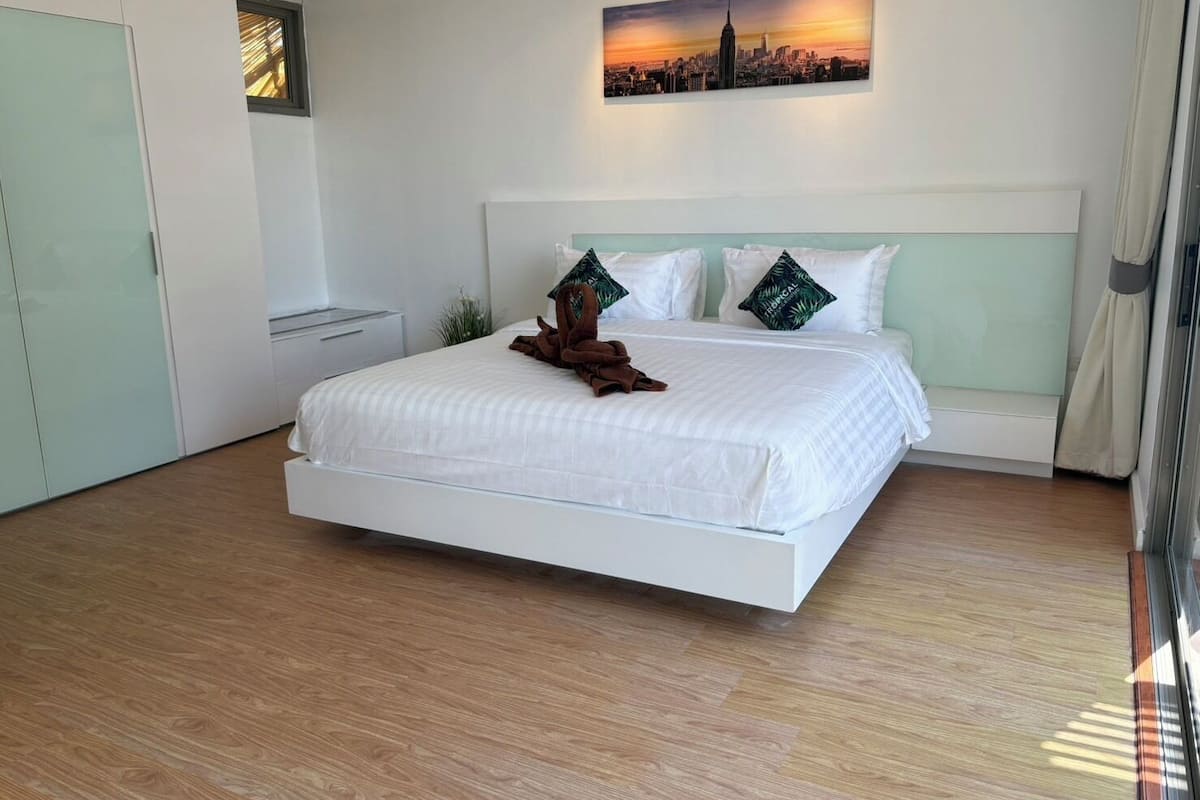 Une chambre d’hôtel moderne avec un grand lit, un tableau représentant un paysage urbain au-dessus du lit et une vue sur la ville par la fenêtre.
