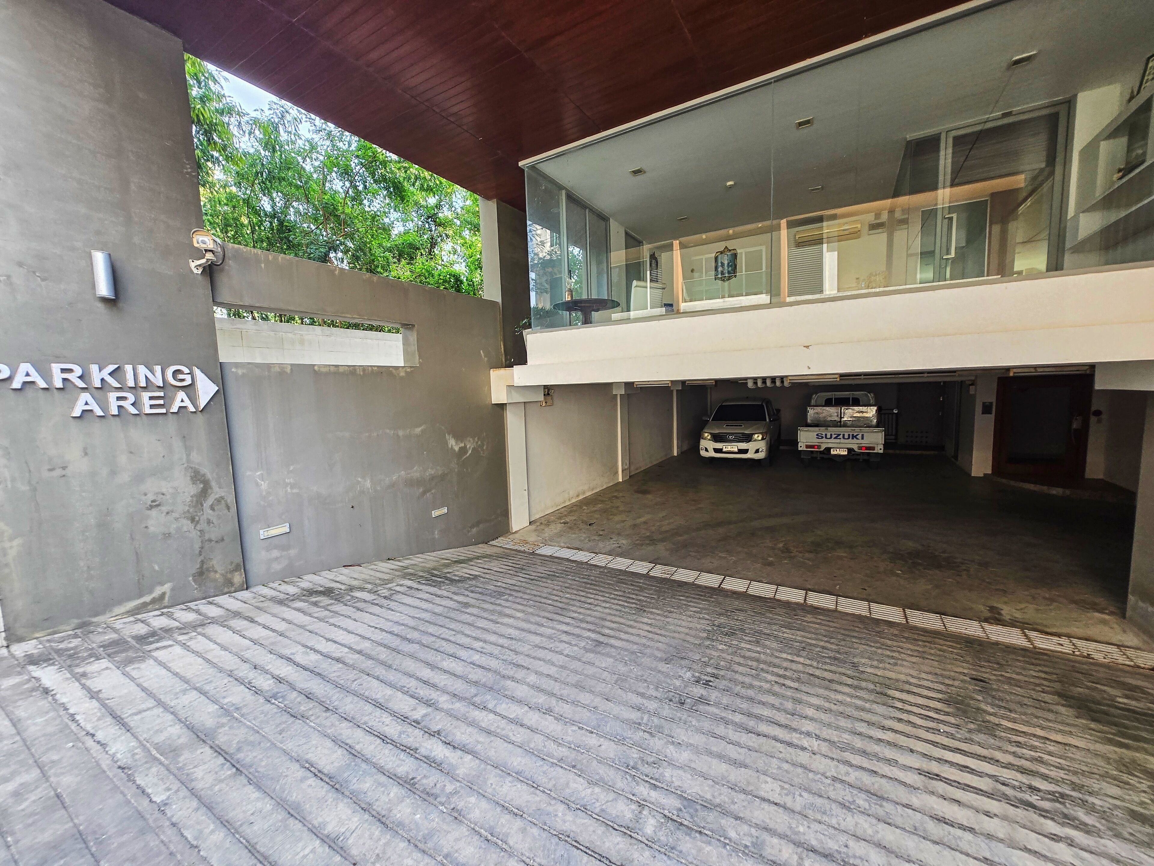 A modern building with a covered parking area, a concrete wall with a 'PARKING AREA' sign, and a Suzuki truck parked inside.