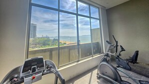 A room with a large window offering a view of a beach and cityscape. - Avatara Beachfront - Best Rooftop Pool & Ocean Views (Pattaya)