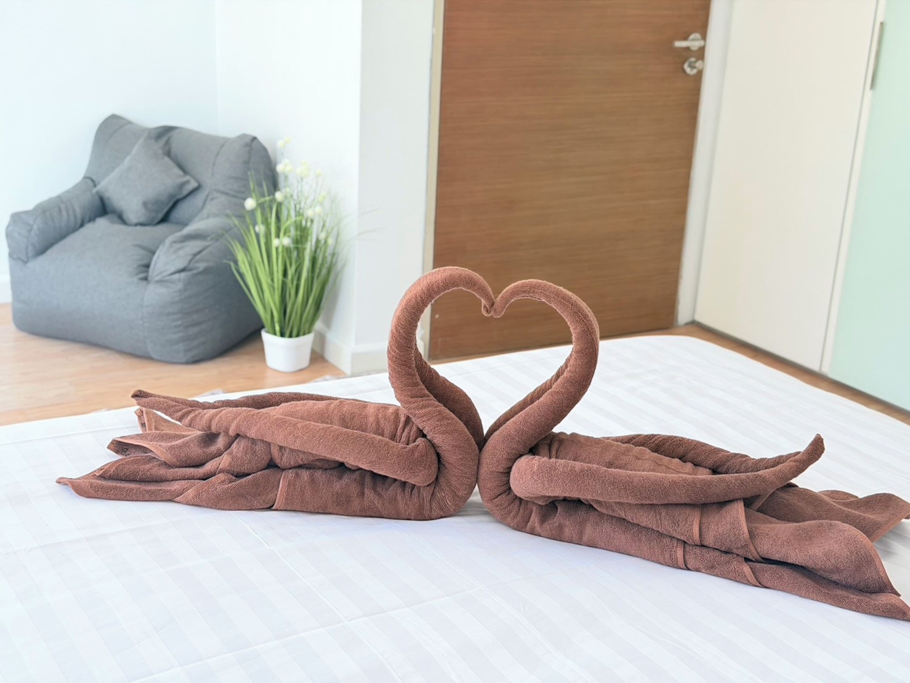 A room with a bed, a grey bean bag chair, a potted plant, and a wooden door.