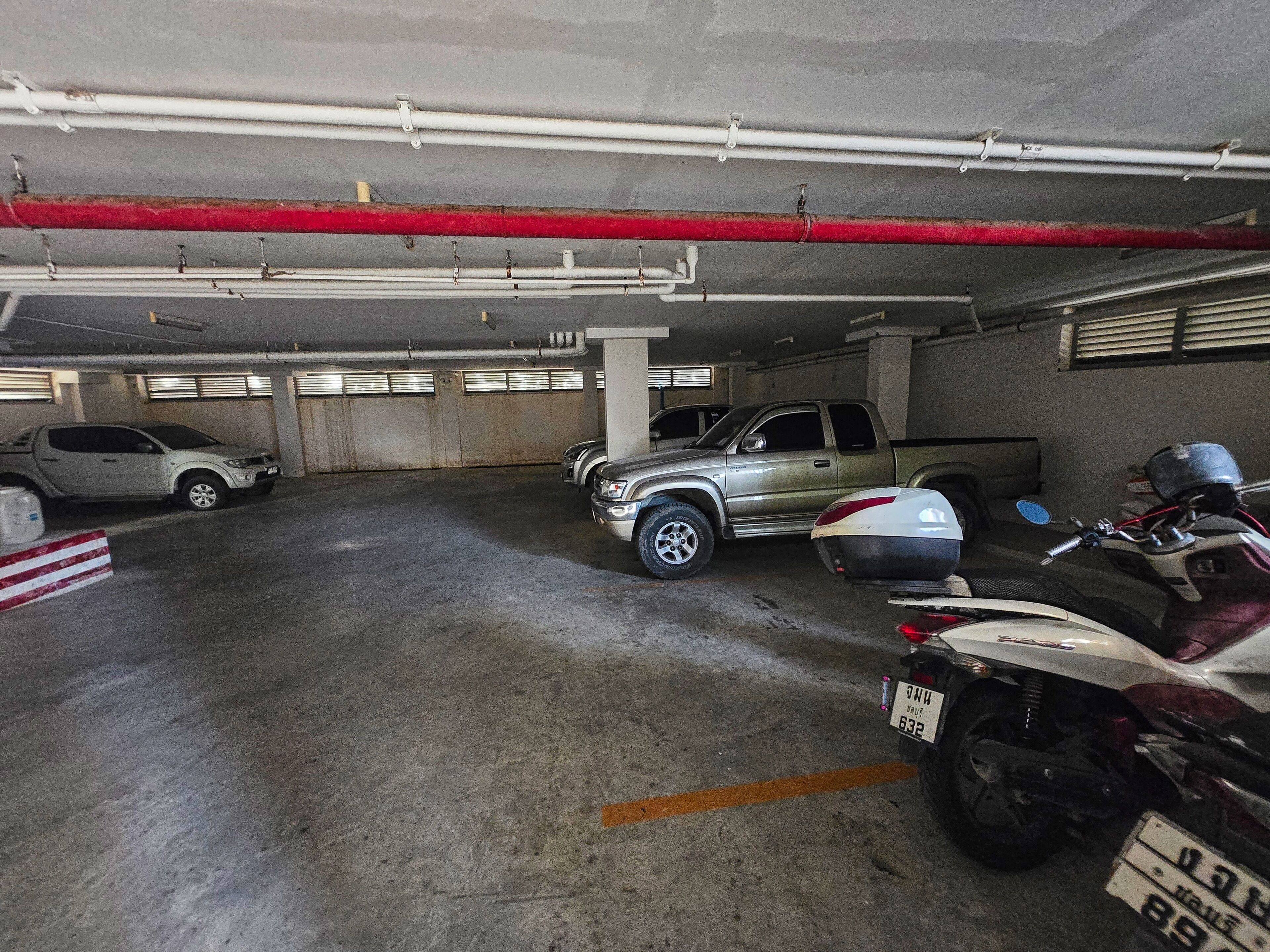 A parking garage with concrete floors, metal pipes, and a red pipe running across the ceiling.