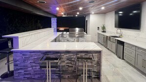 A modern kitchen with a central island, built-in appliances, and a large TV. - Glendora Super House! (Glendora)