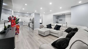 A modern living room with a sectional sofa, a coffee table, and a kitchen area in the background. - Glendora Super House! (Glendora)