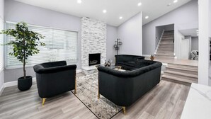 A modern living room with black sofas, a fireplace, and a staircase leading to an upper level. - Glendora Super House! (Glendora)