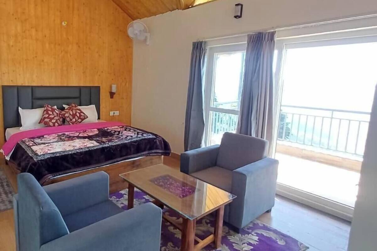 A room with a bed, two armchairs, a small table, and a balcony with curtains.