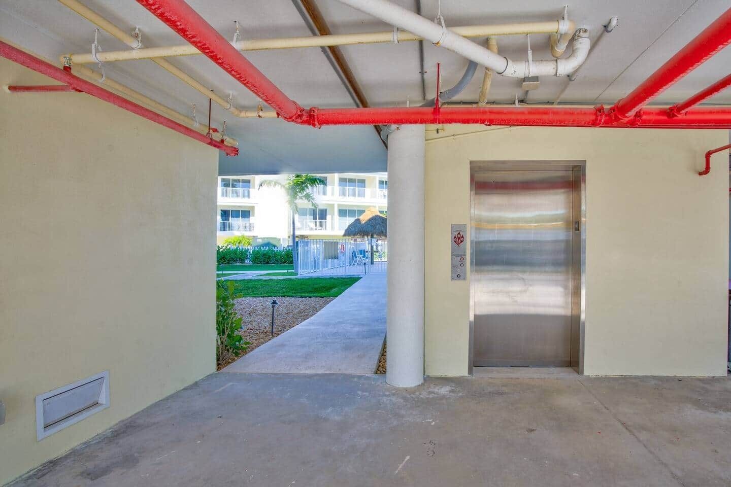 An elevator in a hallway with visible pipes and a concrete floor.