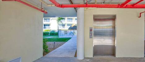 An elevator in a hallway with visible pipes and a concrete floor.
