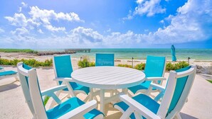 Zona relax in spiaggia con un tavolo rotondo e sedie blu, affacciata sull'oceano e un molo.