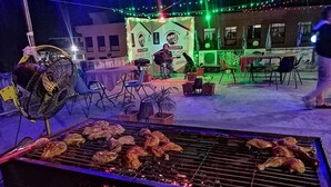 Un coin barbecue avec du poulet grillé, un ventilateur et des sièges d’extérieur.