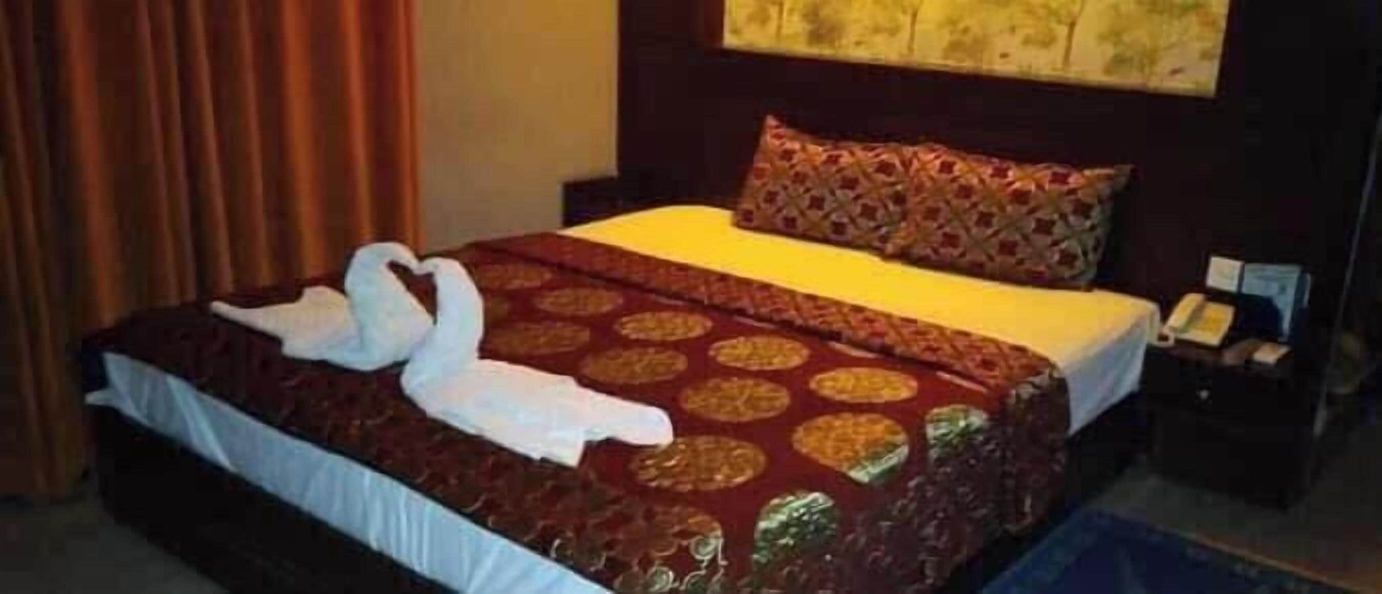 A hotel room with a neatly made bed, a pillow, and a bedside table with a lamp and a book.