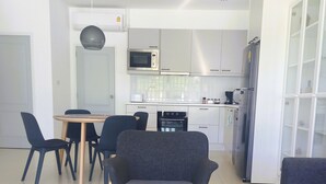 Ett modernt kök med vita skåp, en mikrovågsugn och ett kylskåp. Det finns en matplats med ett bord och stolar.