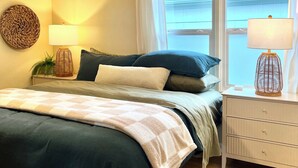 Ein Schlafzimmer mit Bett, Nachttischlampen, Deckenventilator und einem Fenster mit Vorhängen.