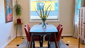 Ein Essbereich mit Tisch, Stühlen, einer Blumenvase, einer Pendelleuchte und einem Fenster mit Jalousien.