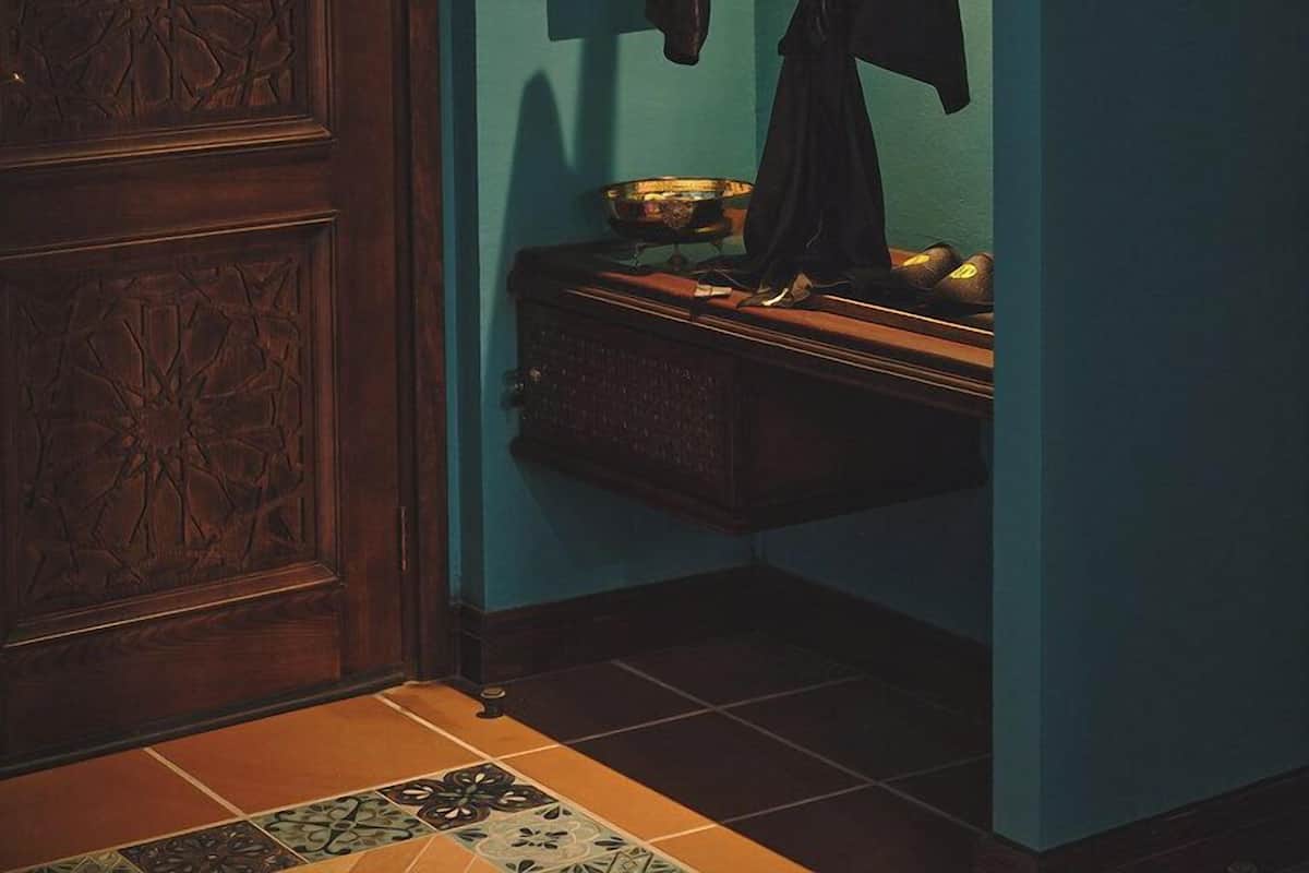 A room with a wooden door, a hanging robe, a small shelf with a bowl, and a tiled floor.