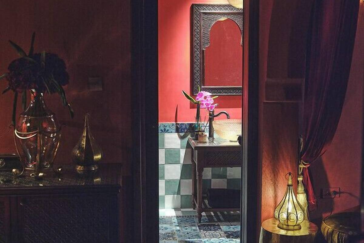 A room with a checkered floor, a mirror with an arch design, a table with a lamp, and a red curtain.