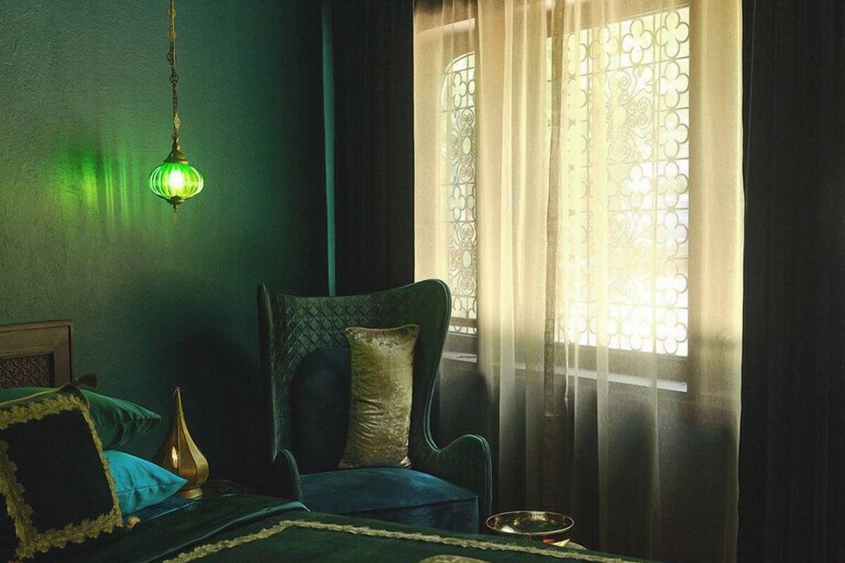 A room with a bed, a chair, a hanging light fixture, and a window with curtains.