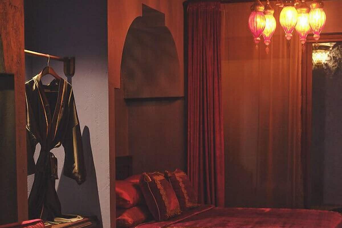 A bedroom with a bed, a chair, a desk, and a hanging light fixture.
