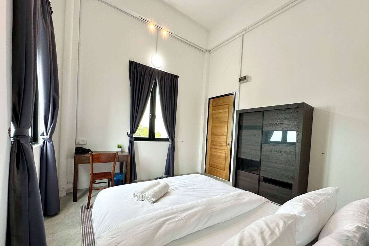 A bedroom with two beds, a wooden wardrobe, a desk with a chair, and a window with curtains.