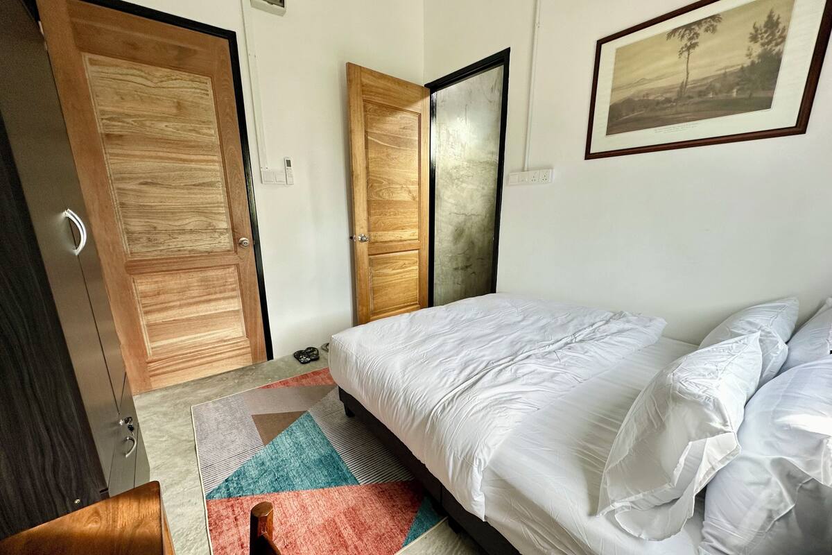 A bedroom with a bed, a wooden wardrobe, a mirror, and a framed picture on the wall.