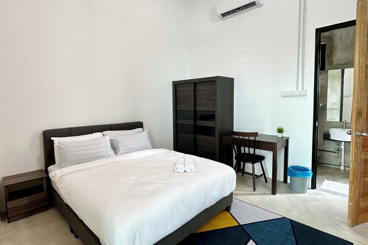 A modern bedroom with a large bed, a desk, and a wardrobe.