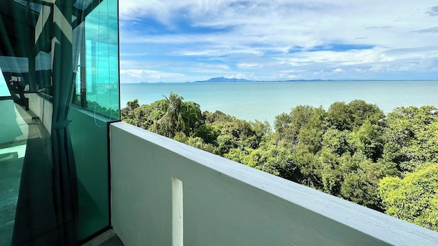 A modern building with a glass facade overlooking a coastal landscape with dense greenery and a clear view of the sea. - Ferringhi Inn 51 (George Town)