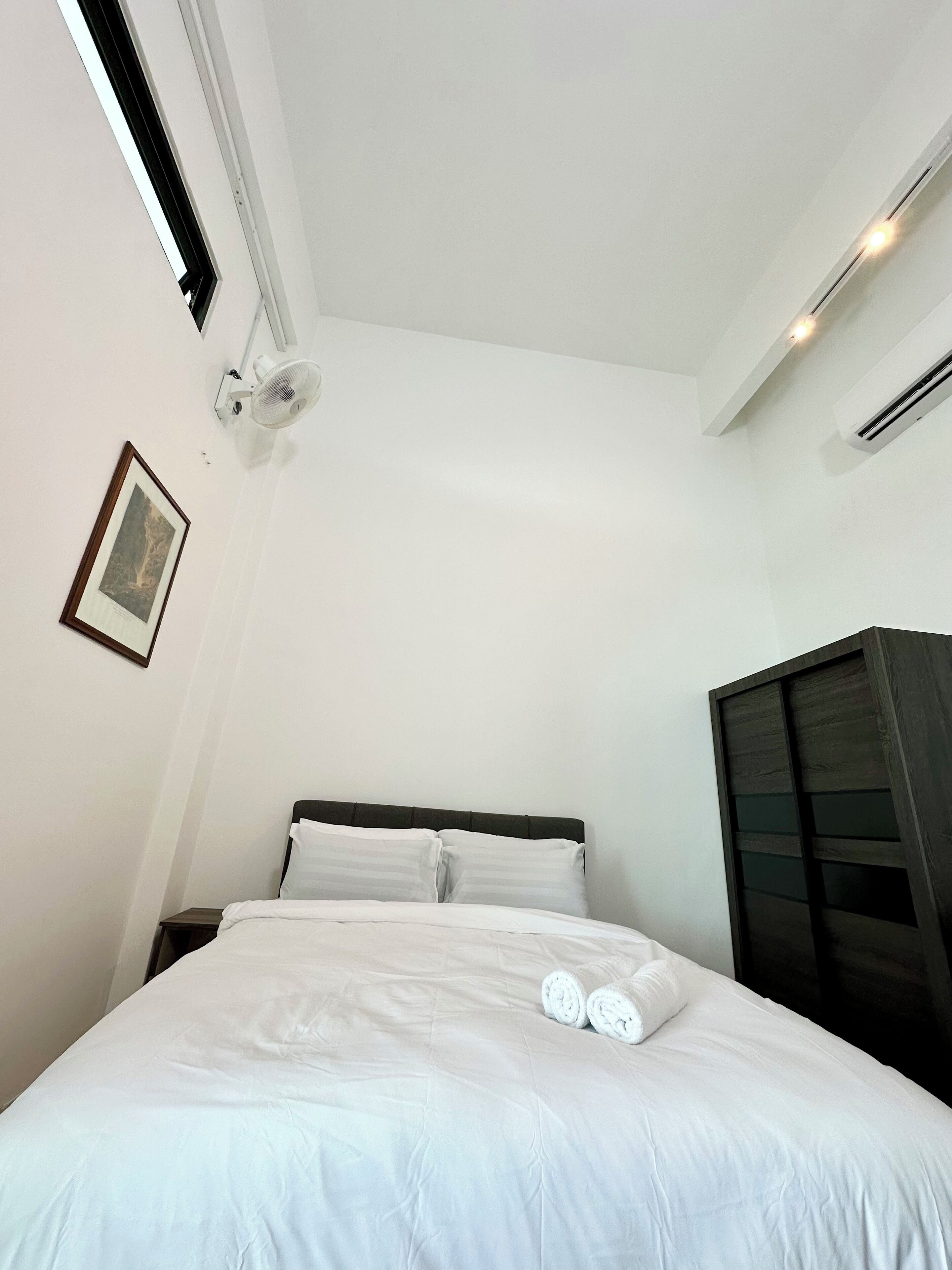 Un dormitorio con una cama, una mesita de noche, un cuadro en la pared y un equipo de aire acondicionado.