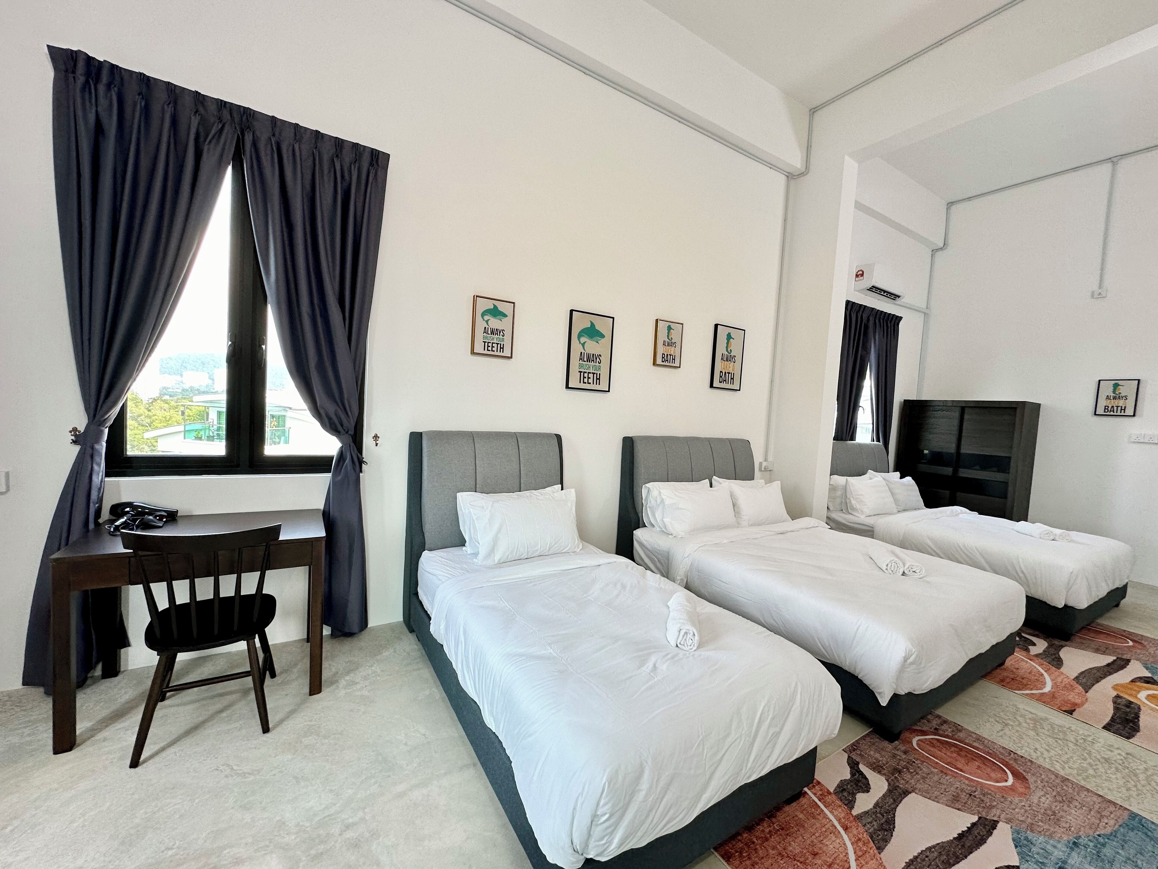 A hotel room with two beds, a desk, and a chair. There are three framed pictures on the wall, and a TV on the right side.