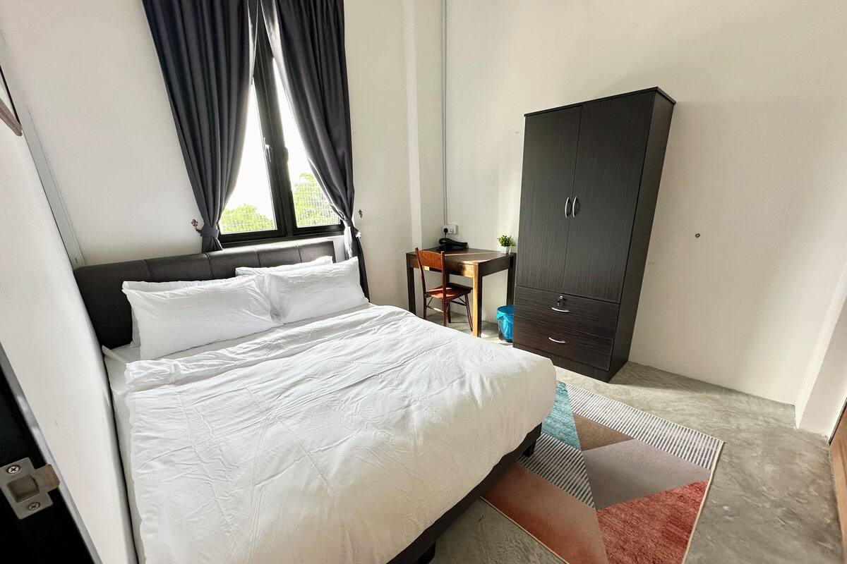 A hotel room with a bed, a wardrobe, a desk, and a window with curtains.