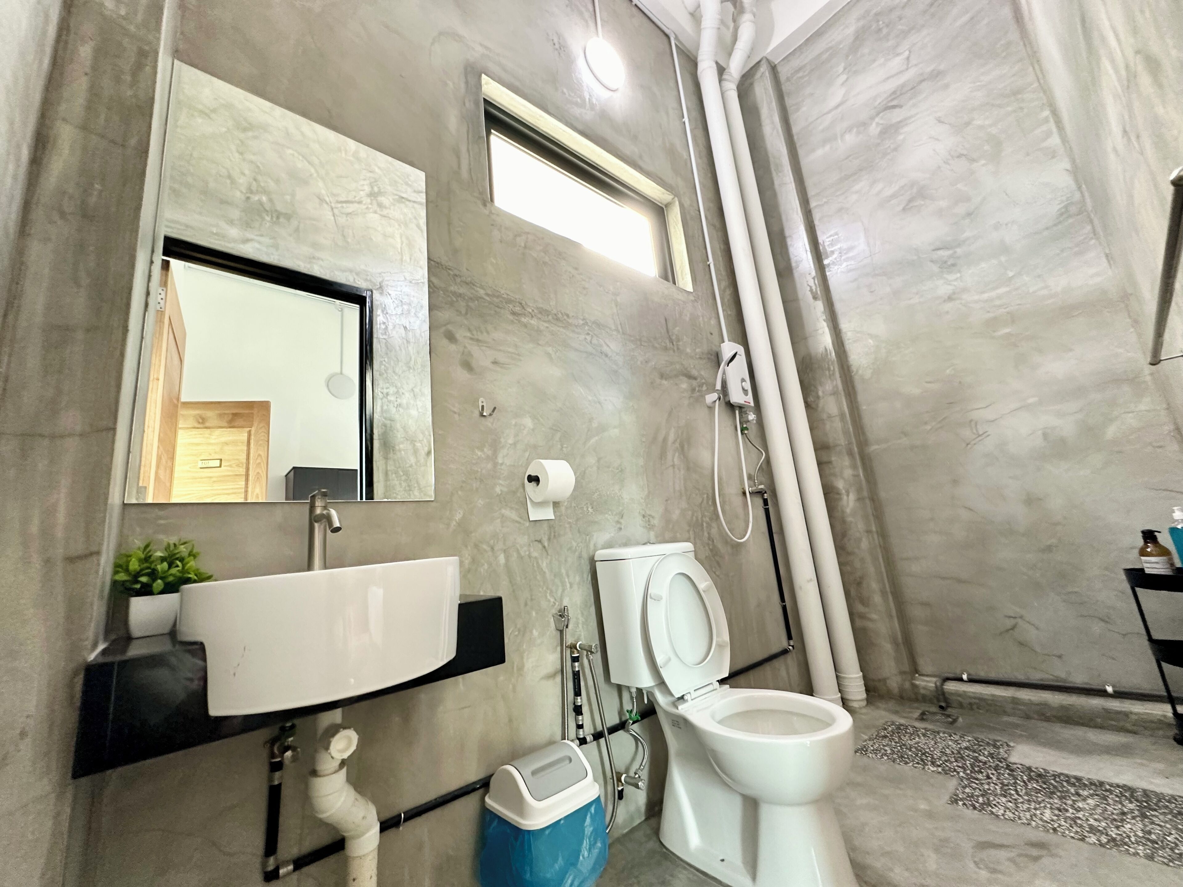 A modern bathroom with a marble wall, a white sink, a toilet, and a shower.