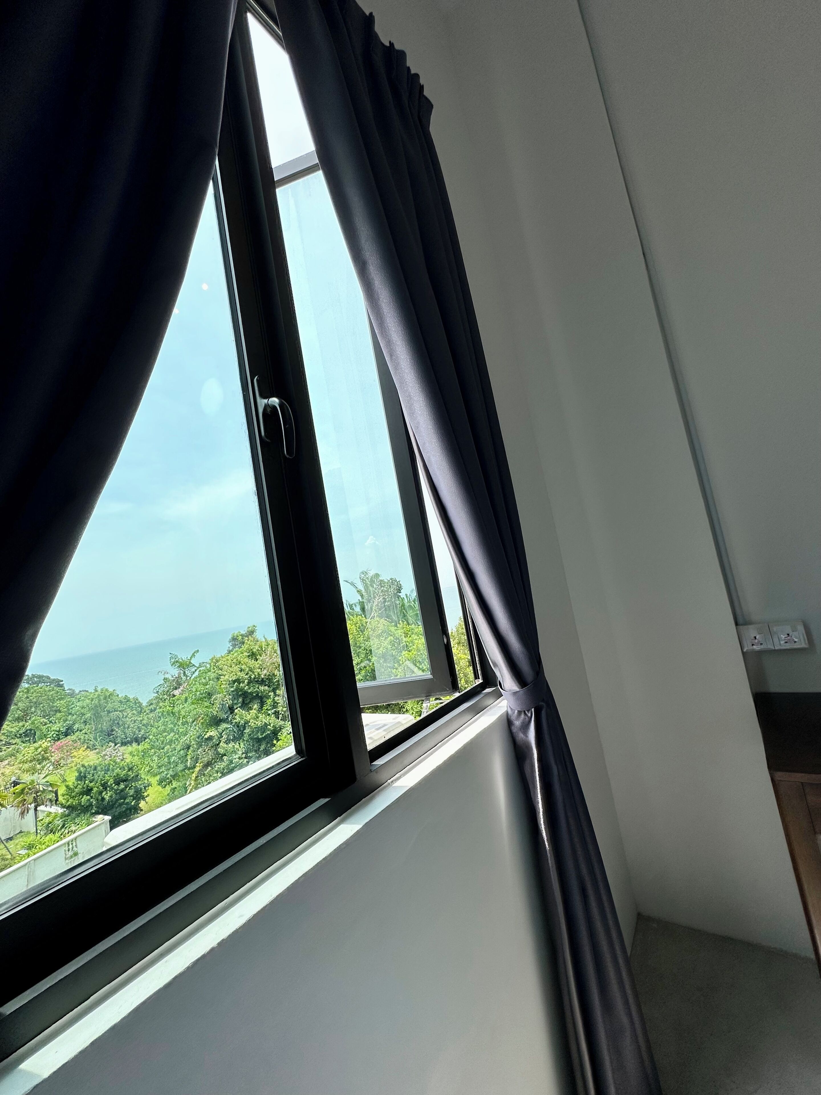 Una habitación con ventana que da a un paisaje verde exuberante y al mar.