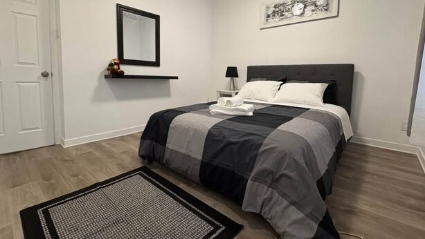 A bedroom with a bed, a nightstand, a lamp, a mirror, and a framed picture on the wall. - Delightful 3-bedroom apartment in Montréal perfect for your stay (Montréal)