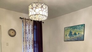 A dining area with a glass table surrounded by four chairs, a decorative hanging light fixture, a clock on the wall, and a landscape painting. - Delightful 3-bedroom apartment in Montréal perfect for your stay (Montréal)