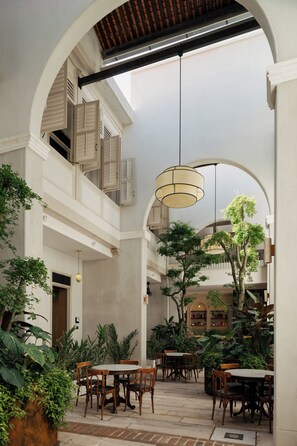 An indoor courtyard with multiple dining tables and chairs, surrounded by lush greenery and a variety of plants. - Cheong Fatt Tze - The Qing Suites (George Town)