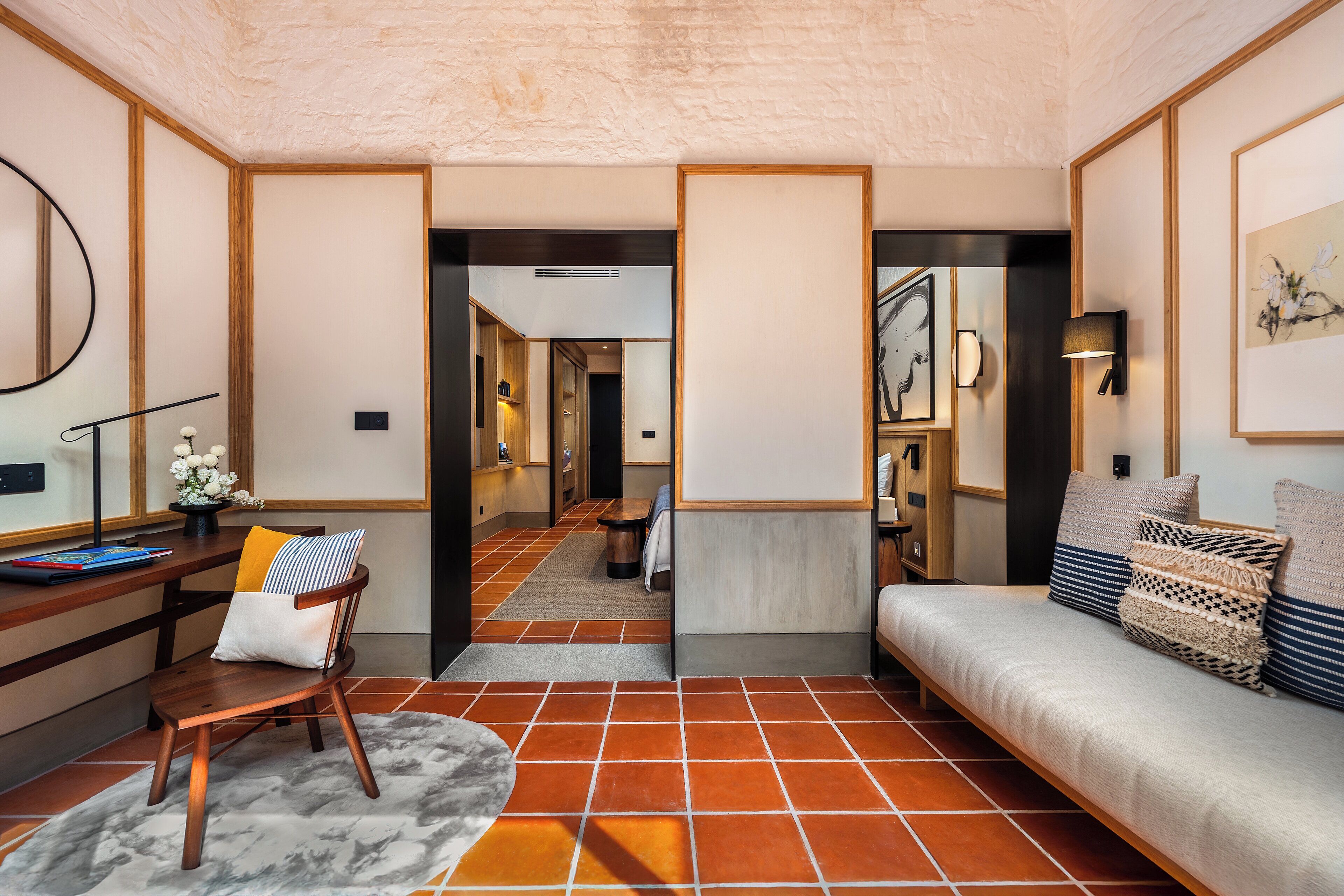 A modern interior with a sofa, a wooden chair, a desk, and a tiled floor.